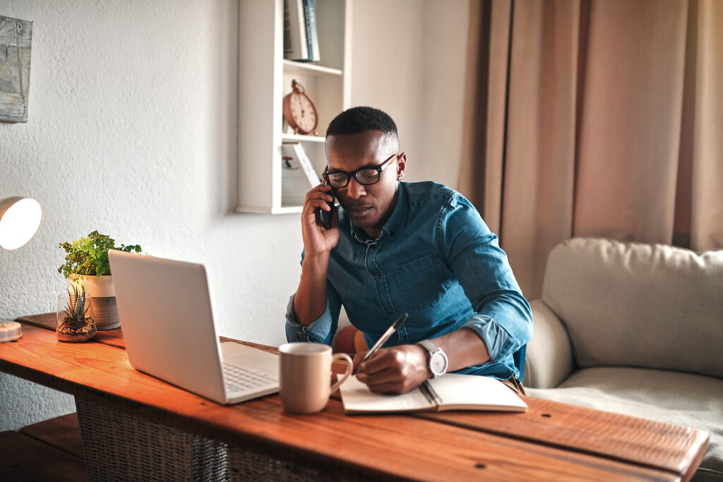 Young entrepreneur on his phone while taking notes at his desk.